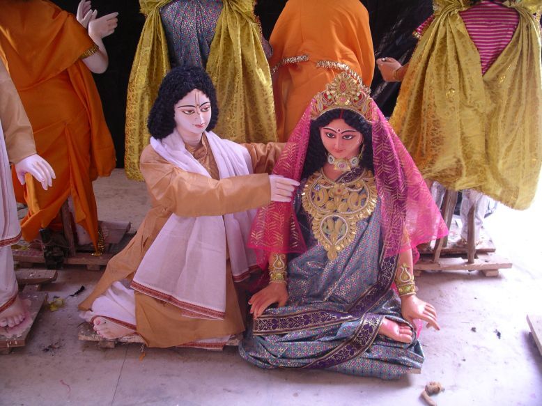 A devotional festival tableau of large, ornately dressed figures representing Sri Chaitanya Mahaprabhu (Gaura) and a richly bejewelled goddess-like female figure, of the kind used in Gaudiya Vaishnava temple pageantry -- shown here for its