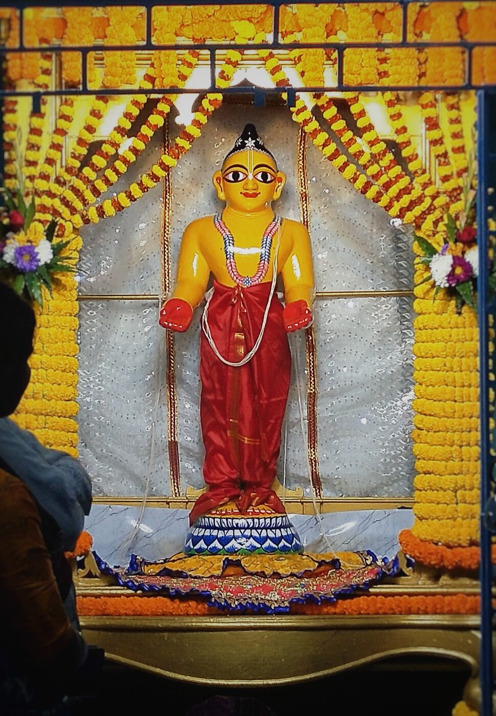 The worshipable deity of Sri Nityananda Prabhu, dressed in his characteristic red cloth and garlanded with marigolds, at Nitai Bari in Nabadwip, West Bengal.