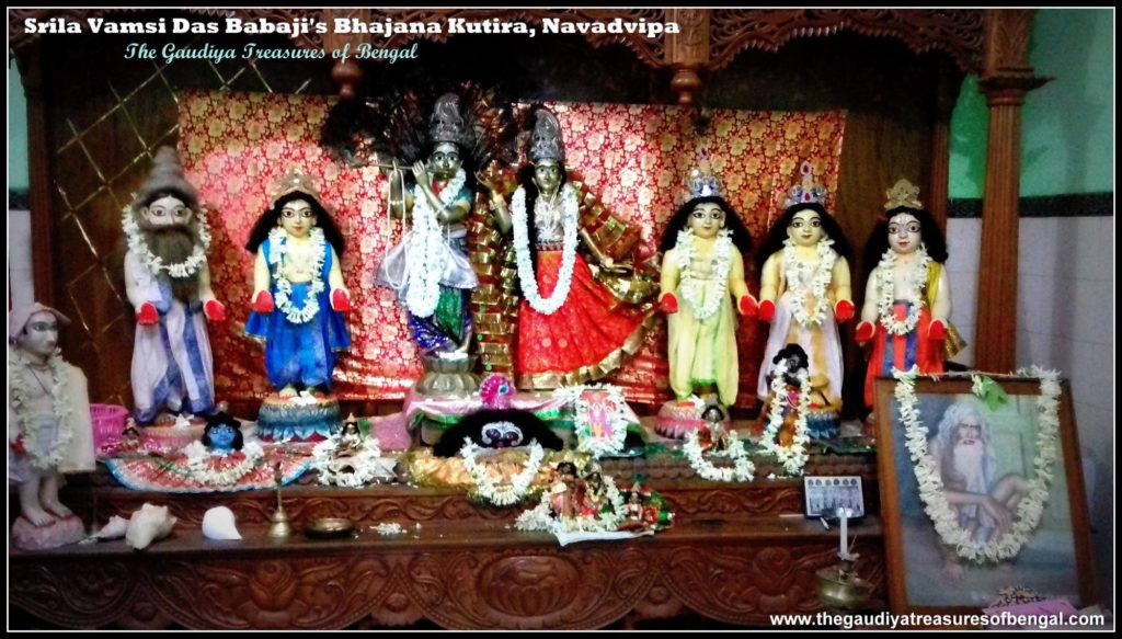 The present-day deity altar inside Sri Vamsi Dasa Babaji's bhajana kutira, showing Gaura-Nitai, Radha-Govinda, and Jagannatha-Baladeva-Subhadra deities, with a garlanded painted portrait of an elderly sadhu (believed to depict Vamsi Dasa Ba